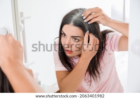 Stressed woman with graying hair looking in mirror Royalty-Free Stock Photo #2063401982