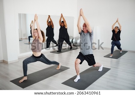 Group of senior people practicing yoga with the coach, they standing on exercise mats in yoga pose and stretching