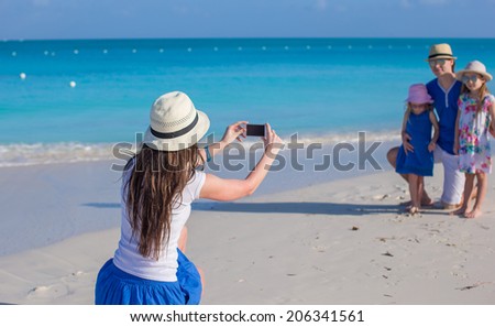 Young mother making photo on phone of her family at the beach