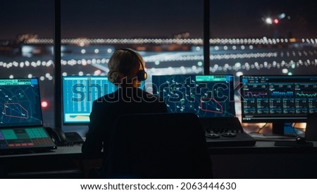 Female Air Traffic Controller with Headset Talk on a Call in Airport Tower at Night. Office Room is Full of Desktop Computer Displays with Navigation Screens, Airplane Flight Radar Data for the Team. Royalty-Free Stock Photo #2063444630