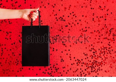 the concept of black friday. black bag in hand on a red background with space for text. High quality photo with copy space