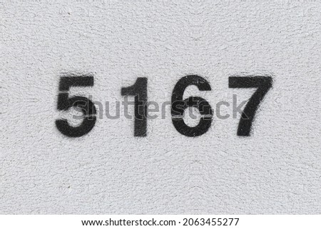 Black Number 5167 on the white wall. Spray paint. Number five thousand one hundred and sixty seven.