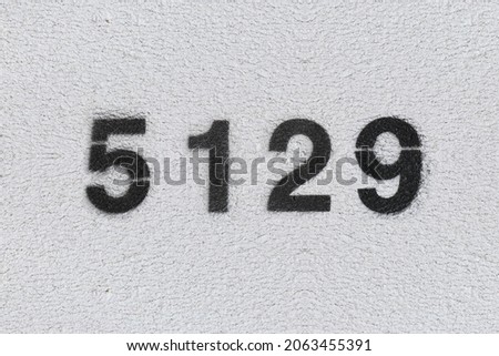Black Number 5129 on the white wall. Spray paint. Number five thousand one hundred and twenty nine.