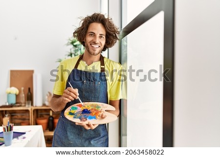 Young hispanic artist man smiling happy leaning on the window at art studio. Royalty-Free Stock Photo #2063458022