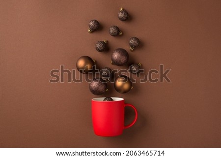 Top view photo of brown and gold christmas tree balls flying out of red cup on isolated brown background