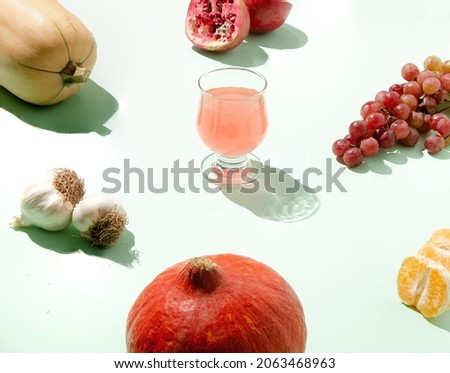 Creative autumn concept idea with pumpkin, grapes, pomegranate, and tangerine on the mint green background. Colorful minimal composition.