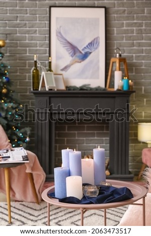 Table with burning candles in interior of living room decorated for Christmas