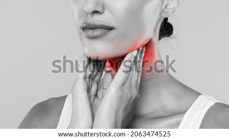 Closeup of sick lady having sore throat, touching her neck with red inflamed zone, suffering from laryngeal disorder, tonsillitis, throat cancer, cold, black and white gray studio background, banner Royalty-Free Stock Photo #2063474525