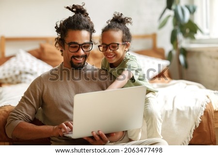 African american father with little son sitting in bedroom at home with laptop and watching cartoons, dad and child looking at notebook screen making video call while enjoying free time together