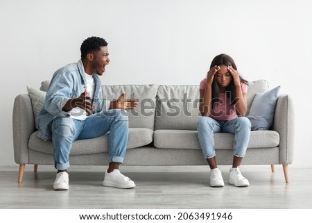 Breaking Up And Divorce Concept. Young married black couple having fight, guy yelling at crying lady, gesturing at home. Furious man shouting at his wife or girlfriend, sitting on sofa at living room Royalty-Free Stock Photo #2063491946