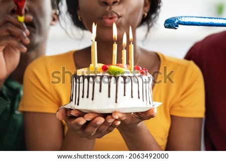 Cropped of black birthday lady holding tasty cake with lit candles and blowing. Unrecognizable african american millennial friends making surprise for girlfriend, closeup. Birthday celebration concept