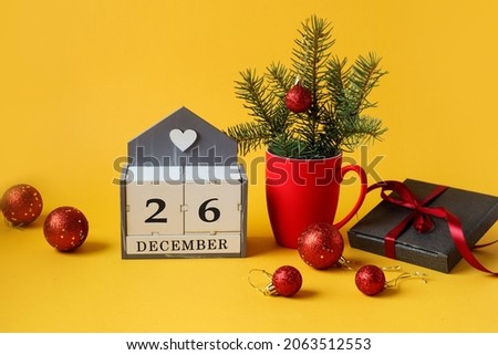 Calendar for December 26 : the name of the month in English, the number 26 ,a Christmas composition in a red cup, Christmas balls, a gift in a gray package, tied with a red ribbon