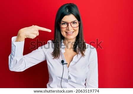Young hispanic woman using lavalier microphone pointing finger to one self smiling happy and proud 