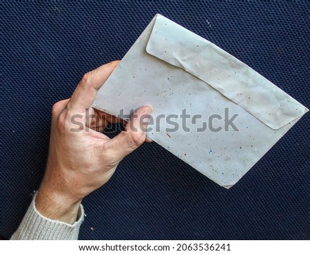 The person holds an old envelope, a letter, with one hand on a blue background.