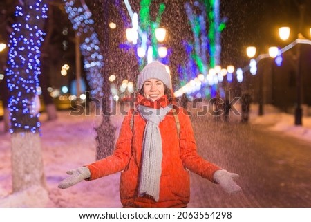 Girl having fun on christmas decoration lights street. Young happy smiling woman wearing stylish knitted scarf and jacket outdoors. Model laughing. Winter wonderland city scene, New Year party.