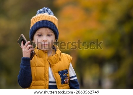 Happy child, playing with phone in the park, calling mommy, autumn pictures taken in the park, children playing