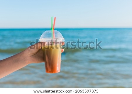 The guy's hand holds a colored chilled non-alcoholic cocktail against the background of the sea.