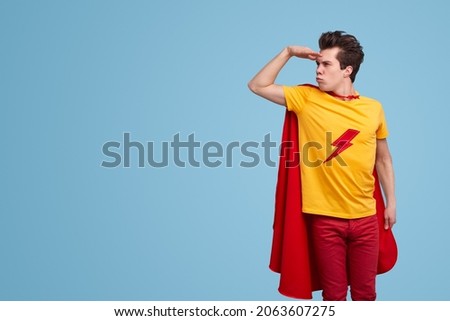 Comic male superhero in vivid cape standing on blue background and attentively looking away