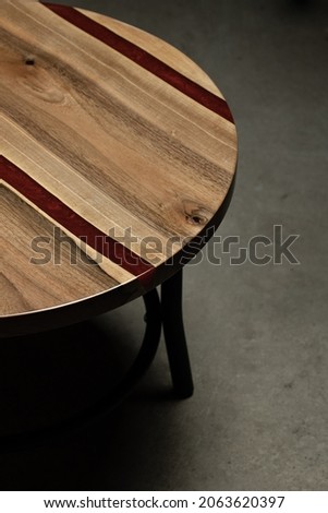 Expensive vintage furniture. The table is covered with epoxy resin and varnished. Luxury quality wood processing. Wooden table on a concrete background. A red epoxy river in a round tree slab.