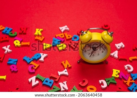 Random colorful alphabet and yellow alarm clock on a red background, colorful letters. Time to school. Study time. Education time.
