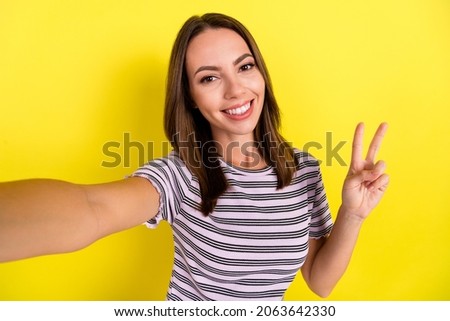 Photo of funny young brunette lady do selfie show v-sign wear white t-shirt isolated on yellow background