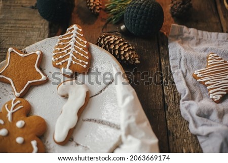 Christmas decorated gingerbread cookies on plate on rustic table with napkin, decorations, spices. Atmospheric moody image. Making stylish christmas gingerbread cookies. Happy Holidays!