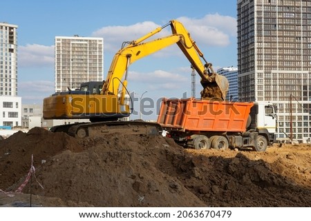 Photo of an excavator and a truck at the construction site of multi-storey buildings in the city.