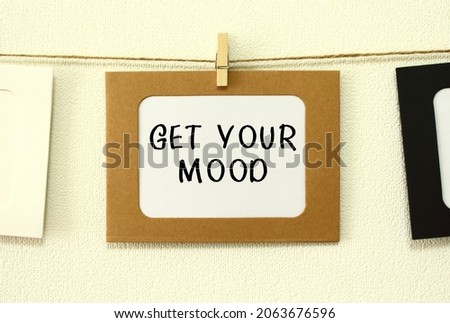 Kraft paper frame hanging on lacing on white wall background with space. In the frame is written the text GET YOUR MOOD.