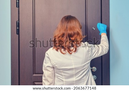 Woman doctor knocks on the door of the apartment when visiting a patient home. Royalty-Free Stock Photo #2063677148