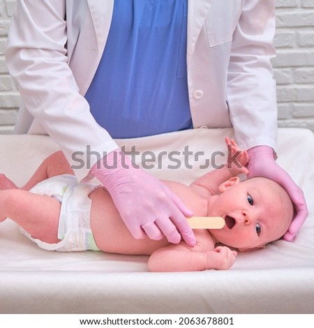 Doctor checks the throat of a newborn child with a plowshare. A nurse in uniform with a wooden stick in her hand examines the child mouth