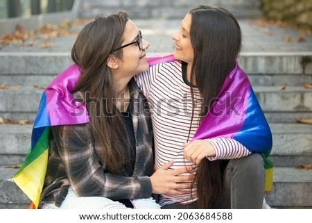 Pregnant Lesbian couple, sitting on stairs hugging with rainbow flag at urban scenery. High quality photo.