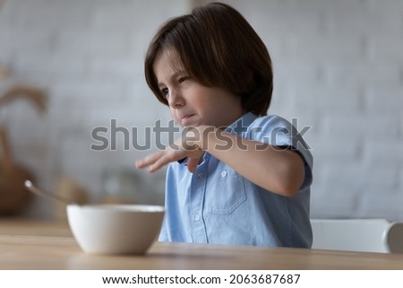 Picky angry eater kid disappointed and disgusted with meal for breakfast, hates healthy food, has no appetite. Emotional boy refusing lunch, turning away from bowl. Children eating behavior disorder Royalty-Free Stock Photo #2063687687