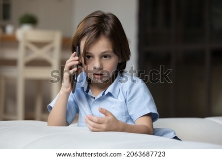Serious gen Z kid making telephone call, talking on mobile phone alone at home. School boy speaking to parent on smartphone, listening. Connection, communication, childhood concept Royalty-Free Stock Photo #2063687723