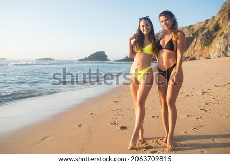 Satisfied friends at beach party. Women in colorful swimsuits, standing at beach, posing, smiling, looking at camera. Party, outdoor activity, friendship concept