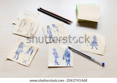 sketches of fashionable silhouette of woman of the XX century hand drawn on sheets of paper on light brown table
