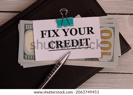FIX YOUR CREDIT - words on a white piece of paper attached to banknotes against the background of a black notebook with a pen. Business concept