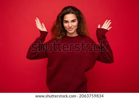 Young beautiful curly brunette woman with sincere emotions poising isolated on background wall with copy space wearing casual dark red sweater. Happy concept
