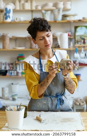 Young sculptor hold sponge shaping jar during pottery workshop. Student learning to work with raw clay in studio. Woman small handmade store owner making kitchenware for sale. Entrepreneurship concept