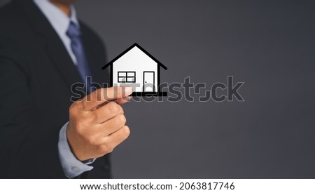 Business and real estate concept. A businessman's holding a mini paper house while standing over gray background. Space for text. Close-up photo. Property insurance and security