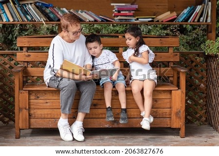 Mature senior grandmother reading a book for his grandchildren small public free library, often called street libraries. Family education time learning, reading book being with kid.