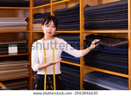 Competent young saleswoman offering various interesting cloth in textile shop. High quality photo