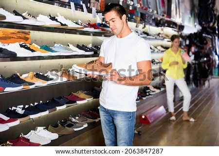 Glad cheerful positive couple of customers choosing male sneakers in showroom