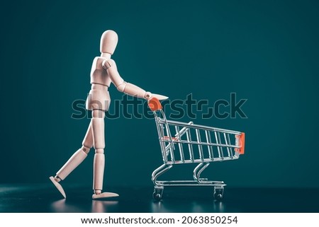 Go shopping concept. Wooden figure with shopping cart on blue background