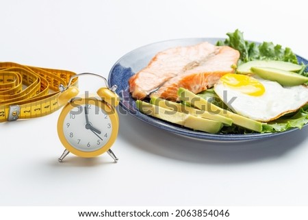 Plate with food, alarm clock and measuring tape on white background.
