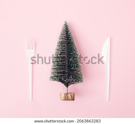 A Christmas and New Year tree with snow  white plastic knife and fork on a pink background. Minimal design. Copy space.