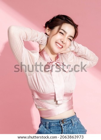 Asian woman with a beautiful face and fresh, smooth skin is dressed in pink. Cute female model with natural makeup and sparkling eyes is smiling and posing on pink isolated background.