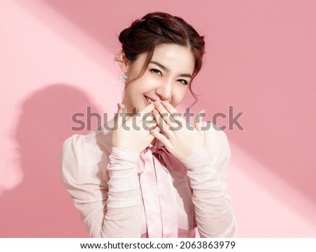 Asian woman with a beautiful face and fresh, smooth skin is dressed in pink. Cute female model with natural makeup and sparkling eyes is smiling and looking at the camera on pink isolated background. Royalty-Free Stock Photo #2063863979
