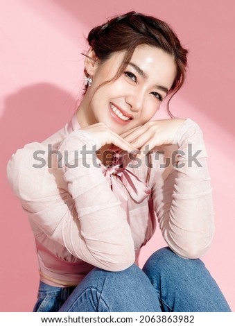 Asian woman with a beautiful face and fresh, smooth skin is dressed in pink. Cute female model with natural makeup and sparkling eyes is smiling and looking at the camera on pink isolated background. Royalty-Free Stock Photo #2063863982