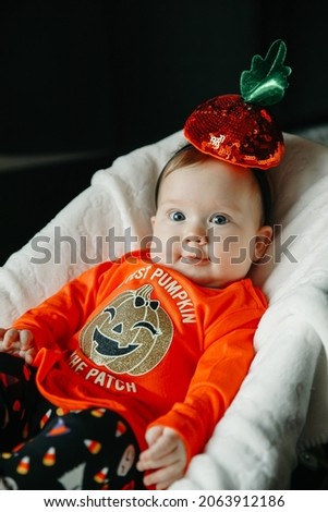 Baby girl in a Halloween pumpkin costume sitting on baby rocking chair
