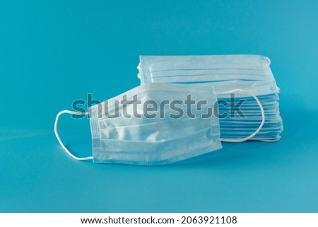 There are many new medical surgical facial three-layer masks stacked high and one mask lies next to the blue background